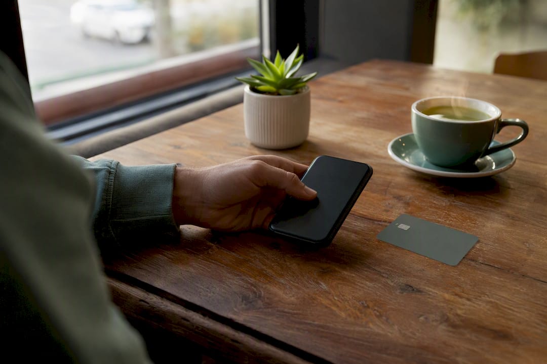 Hand holding smartphone beside credit card on desk